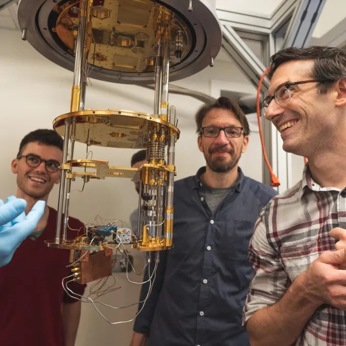 Henriksen (right) inspects a device in the university’s dilution refrigerator laboratory with collaborators from the Center for Quantum Leaps. (Photo: Sean Garcia)